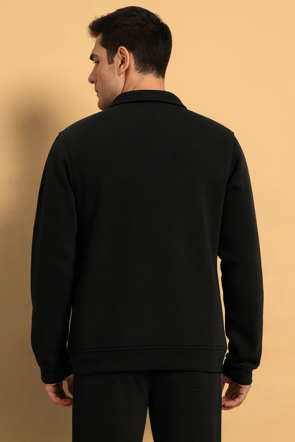 Man wearing black streetwear jacket and pants, back view, beige background
