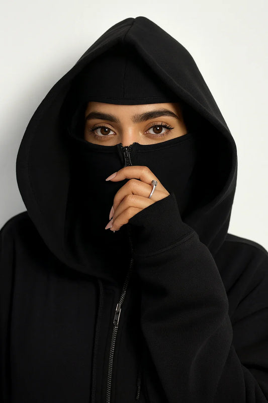 Woman in oversized black streetwear hoodie with hood up and mask covering lower face