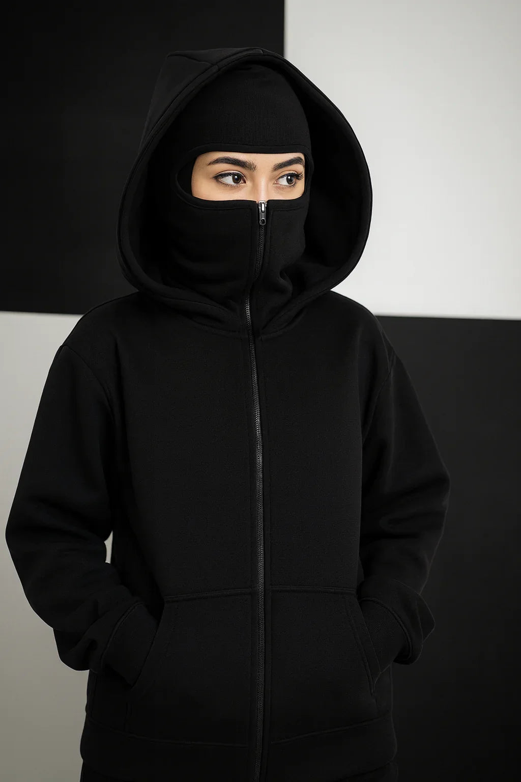 Woman in oversized black zip-up hoodie with hood and face cover, hands in pockets