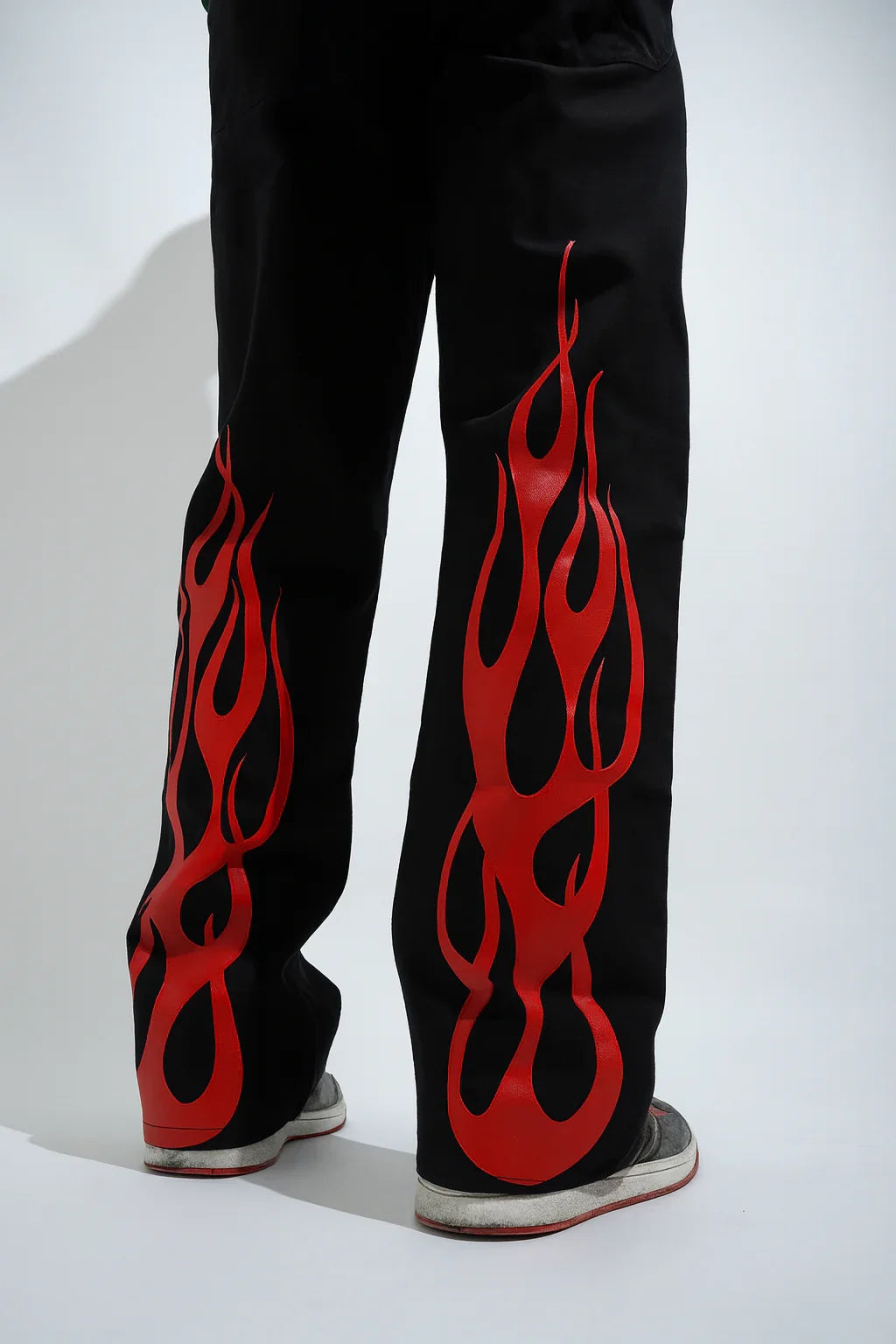 Black streetwear pants with bold red flame graphic on the back, styled with sneakers