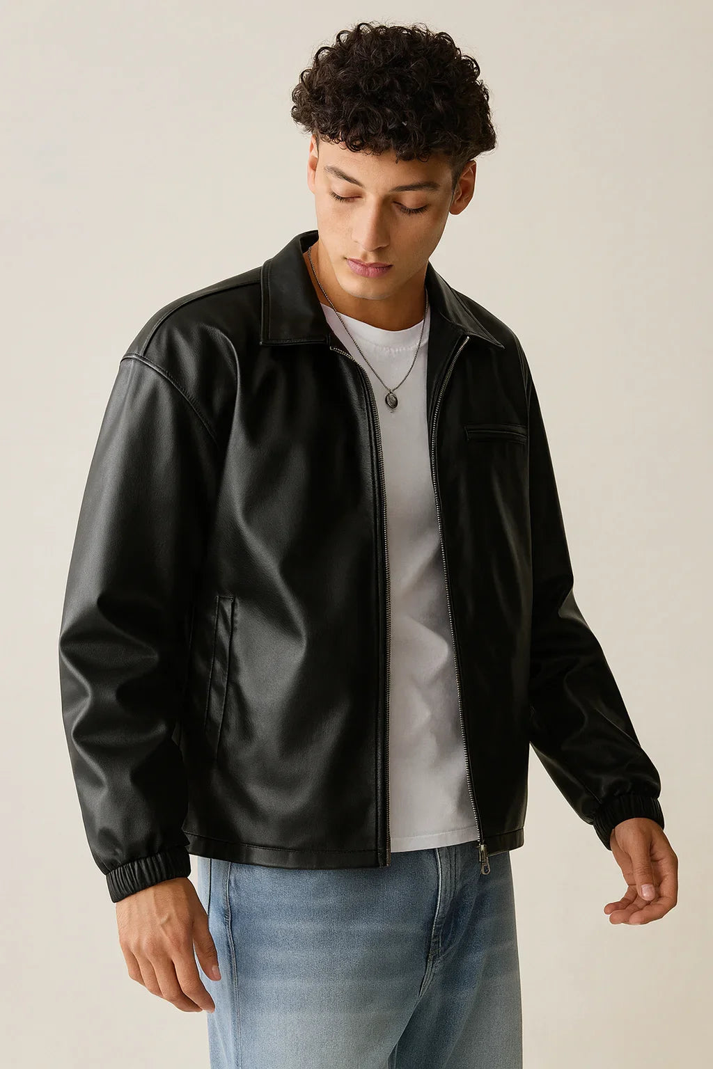 Man wearing black faux leather jacket over white t-shirt and light blue jeans