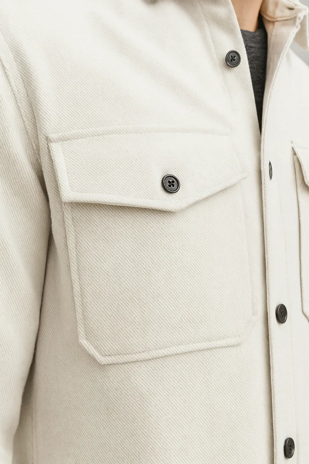 Beige streetwear jacket with buttoned chest pocket and black buttons, close-up view