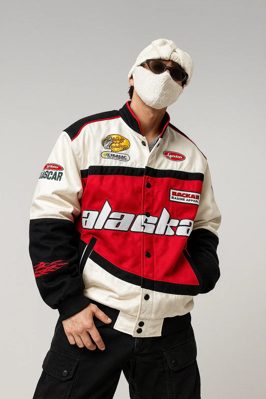 Man in red and white racing jacket with 'alaska' text, black cargo pants, sunglasses, and knit mask