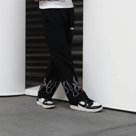 Black streetwear pants with white flame design at hem, styled with black and white sneakers