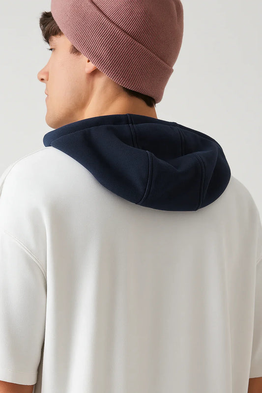 Back view of man in white oversized short sleeve hoodie with navy hood and pink beanie