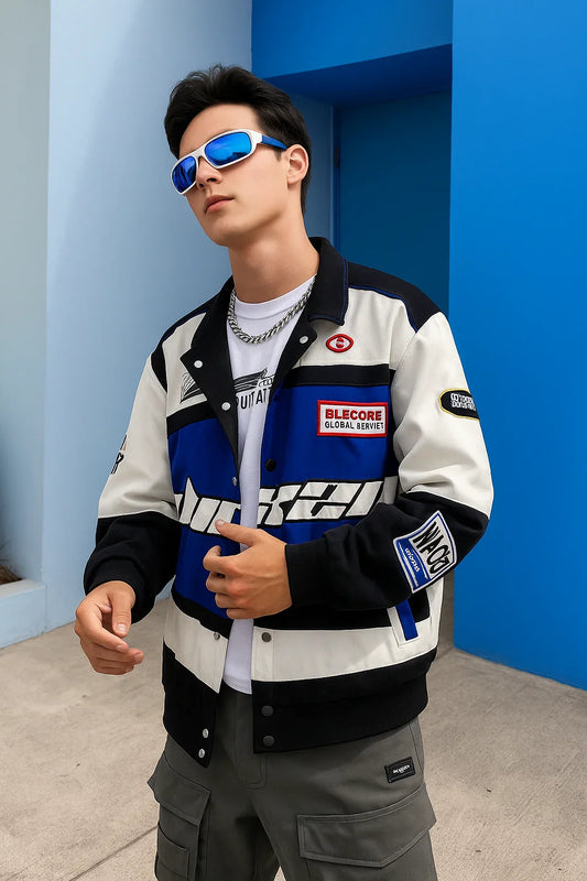 Man in trendy varsity jacket with graphic patches, cargo pants, and blue sunglasses outdoors