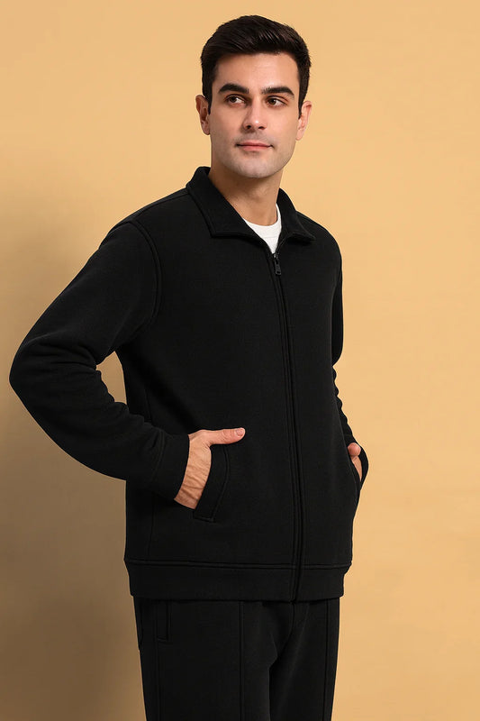 Man wearing black zip-up jacket and pants, hands in pockets, urban streetwear style