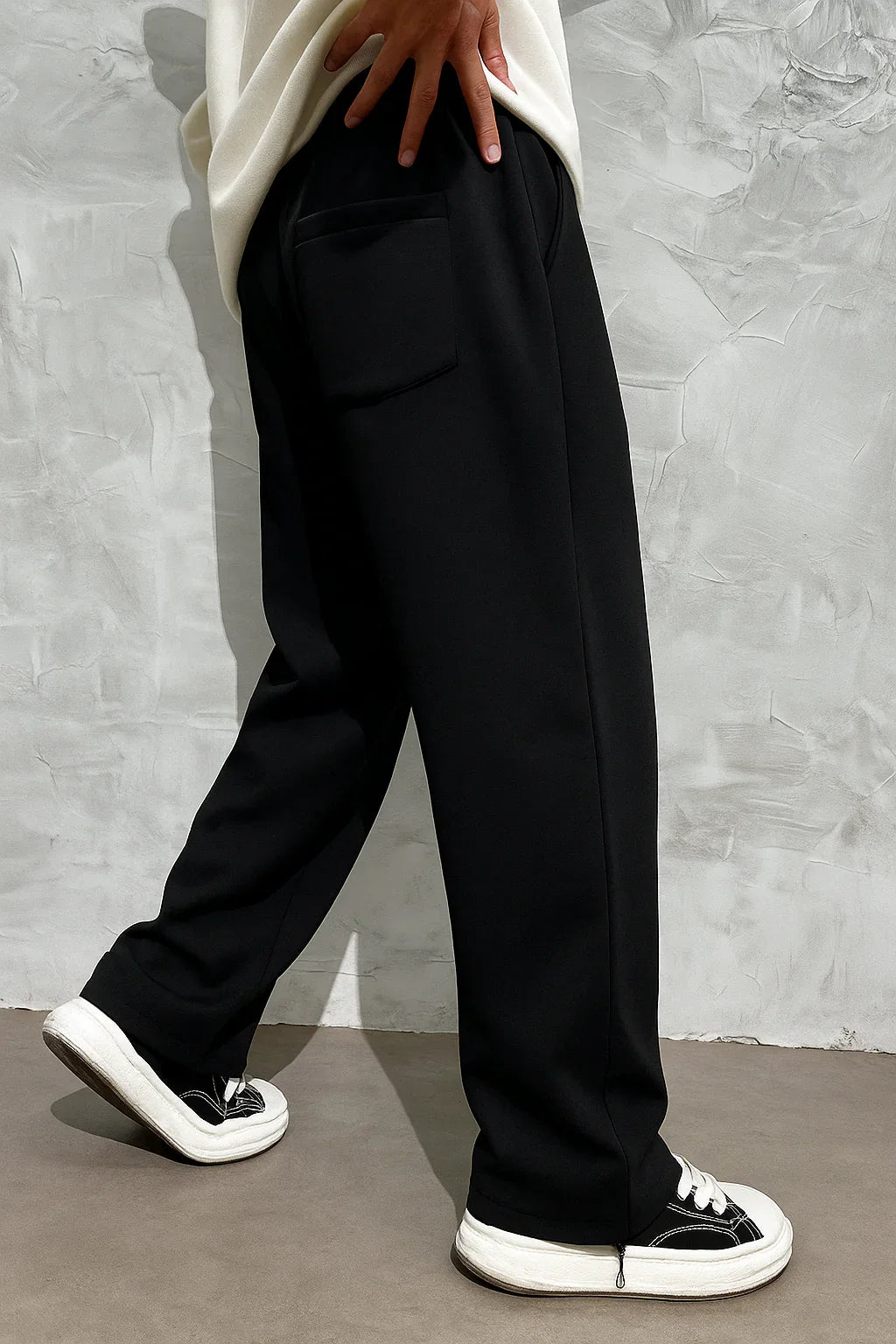 Man wearing black oversized streetwear joggers and white sneakers against textured wall